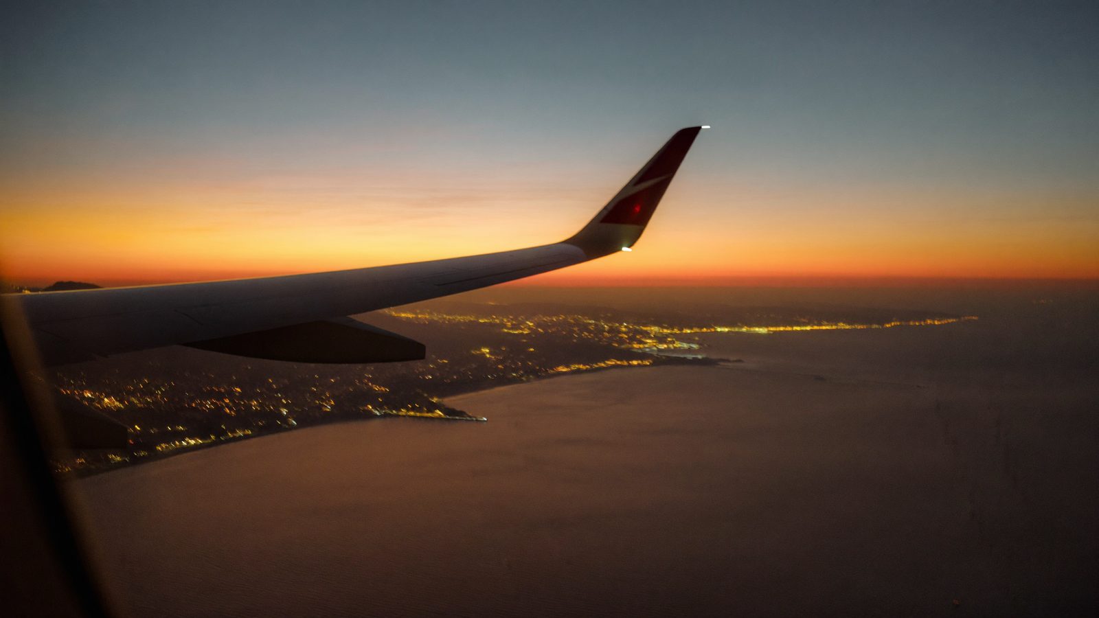 Airplane wing over the Mediterranean coast at sunset — moving money and life from the UK to Spain
